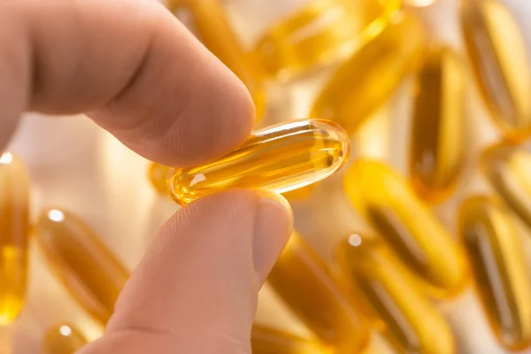 Fingers holding a capsule of cod liver oil, selective focus — Stock Photo, Image
