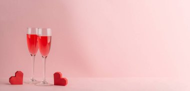İki bardak Prosecco ve pembe arka planda kırmızı kalpler.