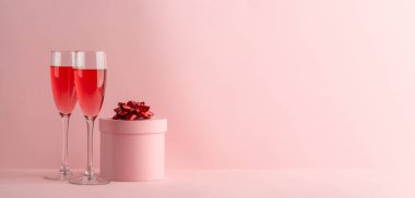 Pembe arka planda iki kadeh kırmızı şarap ve sevgililer günü hediyesi.