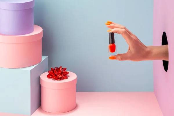 Mão das mulheres segurando um esmalte laranja no fundo azul — Fotografia de Stock