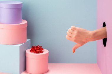 Kadın eli mavi ve pembe arka planda baş parmağını gösteriyor.