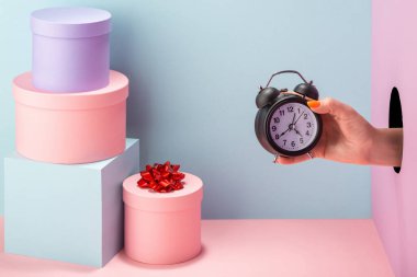 Mavi ve pembe arkaplanda bir çalar saat tutuyor.