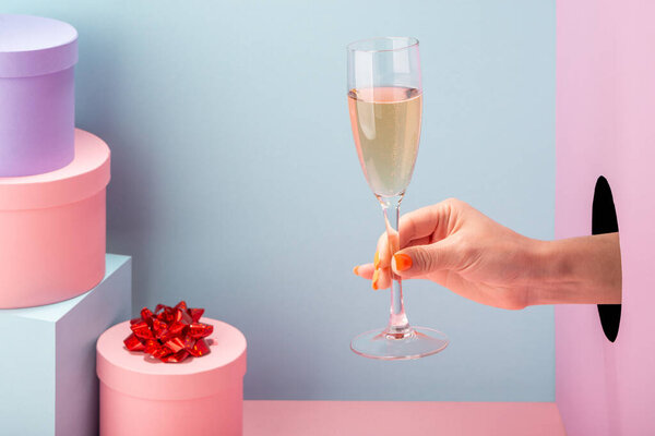 Female hand holding a glass of sparkling wine on blue and pink background