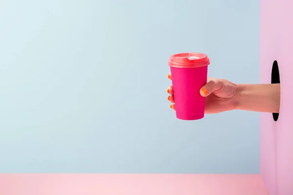 Γυναικείο χέρι κρατώντας ένα ροζ χάρτινο φλιτζάνι καφέ σε μπλε και ροζ φόντο — Φωτογραφία Αρχείου