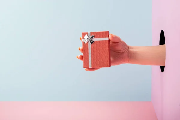 Mão das mulheres segurando uma caixa de presente em fundo azul e rosa — Fotografia de Stock