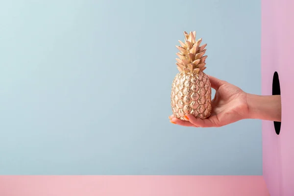 Mão segurando um abacaxi dourado em fundo azul e rosa — Fotografia de Stock