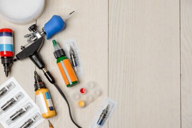 Dövme makinesi, iğneler, beyaz tahta masa üzerindeki mürekkep şişeleri.