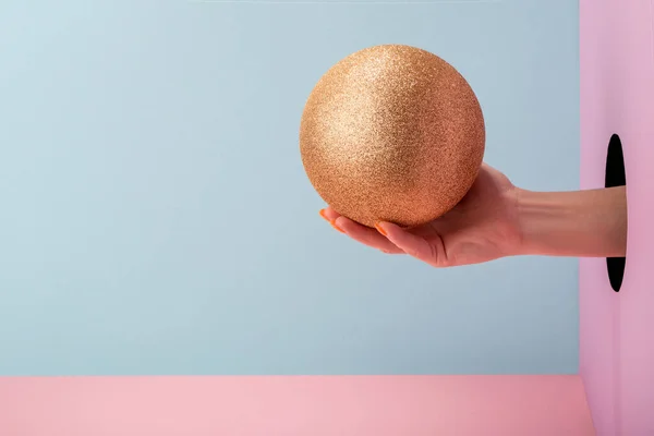 Mão das mulheres segurando uma bola dourada glitter no fundo rosa e azul — Fotografia de Stock