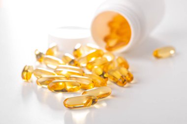 Sarı kapsüller beyaz arka planda bir şişeden yayılmış.