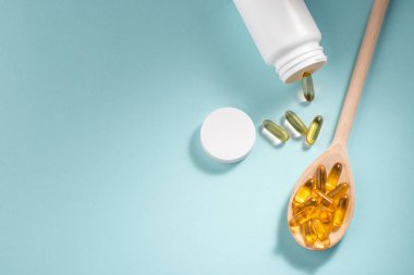 Beyaz şişe sarı kapsül ve mavi arka planda tahta kaşık.