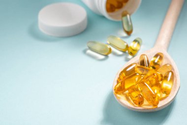 Sarı kapsüller bir şişe ve kaşıktan dağılmış.