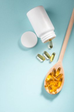 Beyaz şişe sarı kapsül ve mavi arka planda tahta kaşık.