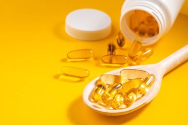 Turuncu arka planda beyaz bir şişeden tahta kaşık Omega-3 kapsülleri.