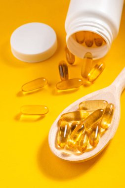 Bir şişe ve kaşıktan saçılmış morina yağı kapsülleri.