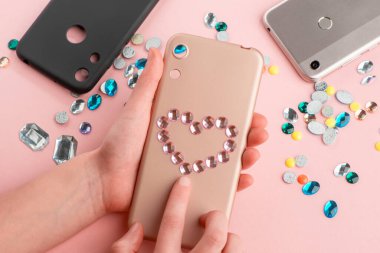 Bej telefon kılıfına pembe elmaslar takan kız.