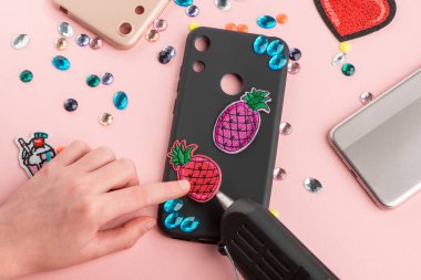 Siyah telefon kılıfını yapay elmaslar ve ananas parçalarıyla dekore eden bir kız.