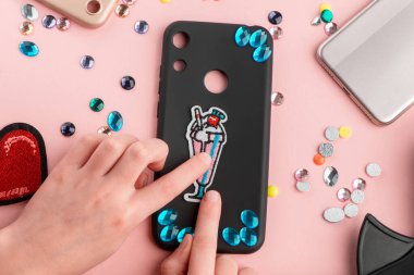 Siyah telefon kılıfını yapay elmaslar ve işlemeli bantlarla süsleyen bir kız.