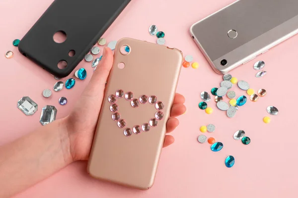 Girl put a rhinestone heart onto beige phone case — Stock Photo, Image