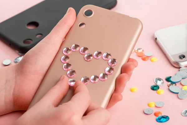 Girl attaching pink rhinestone heart onto beige phone case. — Stock Photo, Image