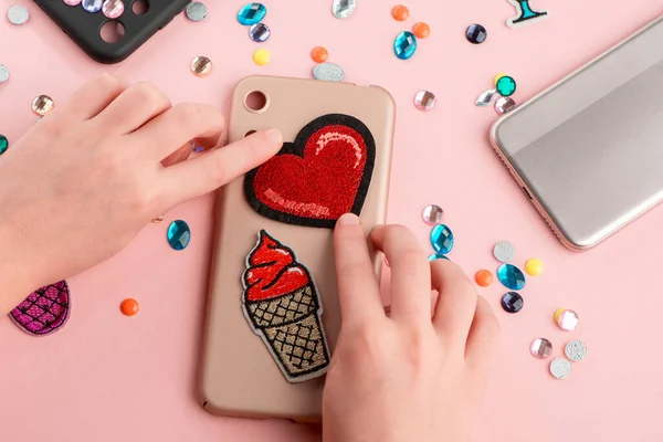 Girl putting red heart and ice cream patches onto beige phone case — Stock Photo, Image