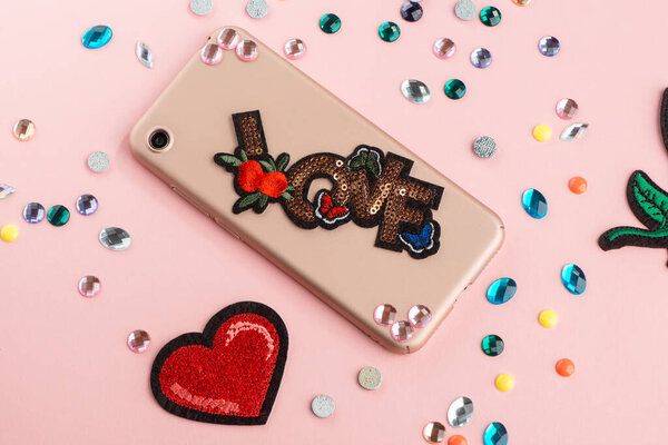 Girl attaching rhinestones and embroidered patch onto beige phone case