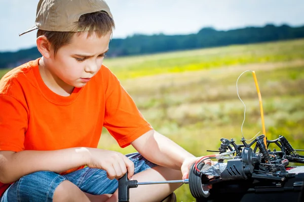 Ragazzino repaire la radio auto di controllo all'aperto vicino campo — Foto Stock