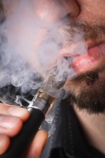 Jeune homme fumant cigarette électronique sur fond noir — Photo