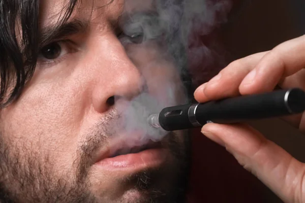 Молодой человек курит электронную сигарету на черном фоне — стоковое фото