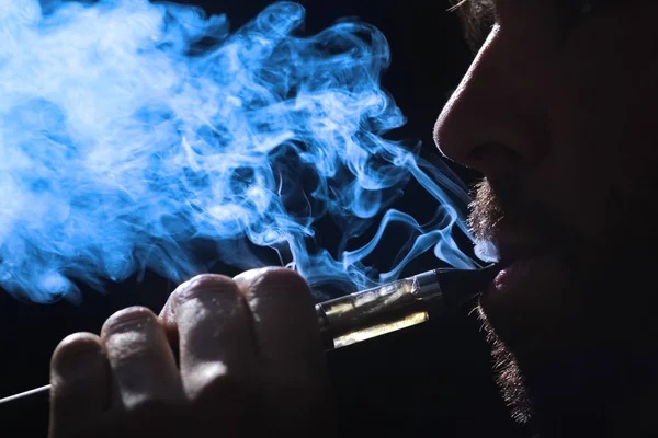 Молодой человек курит электронную сигарету на черном фоне — стоковое фото