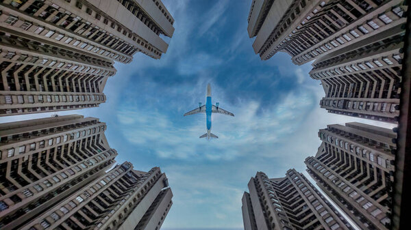 Airplane flying over skyscraper on bright blue sunny day taken from low angle