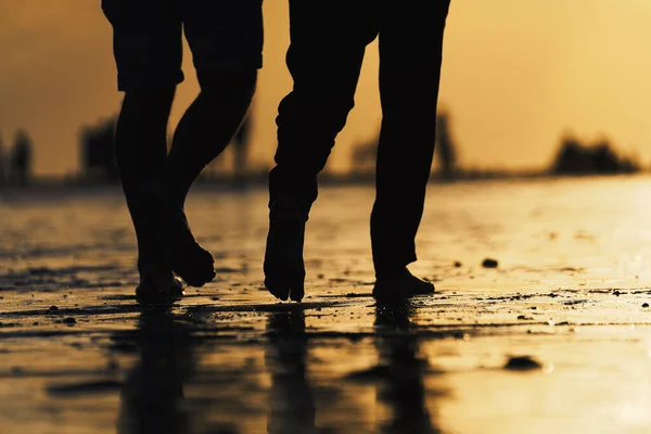 Silhouette of two people legs and feet walking on the beach and its reflection in the wet sand during the sunset