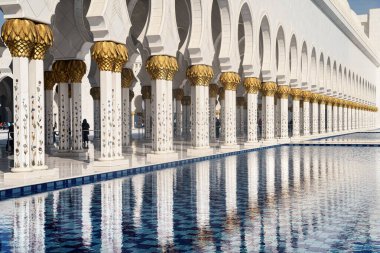 Güneşli bir günde Abu Dabi Camii 'nin beyaz kolonları havuz suyuna yansıdı..