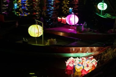 Üzerinde renkli Çin fenerleri olan Asya teknesi gece vakti suya ışığını yansıtıyor.