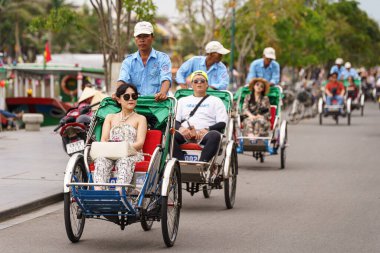 Gündüzleri insanları pedallı taksiyle Hoi caddelerinde taşıyan adamlar.