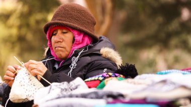 Yerli kadın, sokakta renkli giysilerle dokuyor.