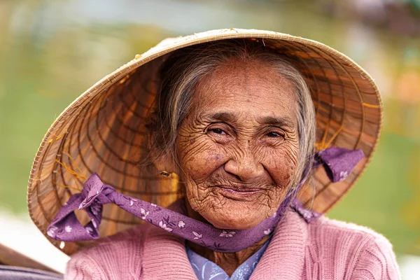 Vietnamlı yaşlı kadın menekşe süveter ve şapka ile kameraya gülümsüyor.