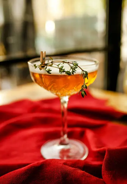 Şeffaf bir bardakta kokteyl, odak noktasındaki kırmızı bir masa örtüsünün üzerinde ince bir bacak.