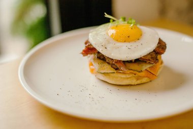 Tahta tuzlu beyaz tabakta yumurtalı peynirli hamburger.