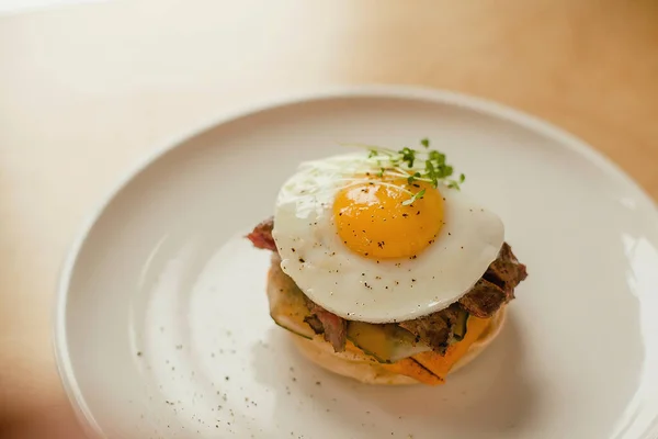 Tahta tuzlu beyaz tabakta yumurtalı peynirli hamburger.