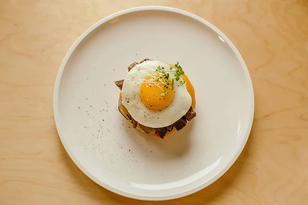 Tahta tuzlu beyaz tabakta yumurtalı peynirli hamburger.