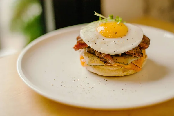 Tahta tuzlu beyaz tabakta yumurtalı peynirli hamburger.