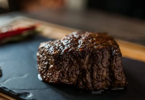 Siyah arka planda biberli sulu biftek. Masa örtüsünün üstünde bir karatahta.