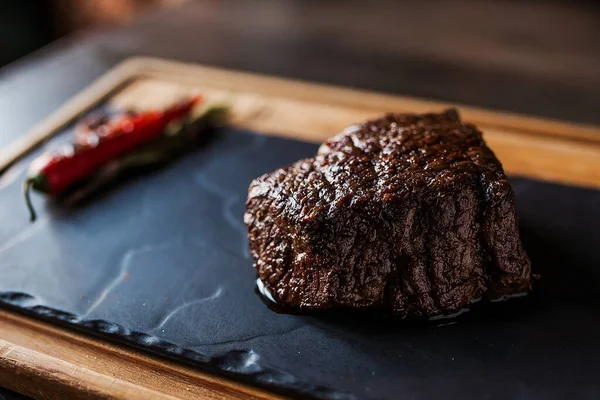 Siyah arka planda biberli sulu biftek. Masa örtüsünün üstünde bir karatahta.