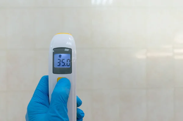 Doktor kızılötesi temas olmayan termometreyi tutuyor. Dijital aygıt normal vücut sıcaklığını Celsius derecesinde gösterir