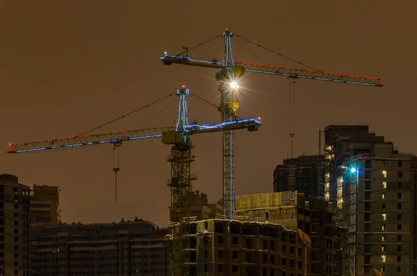 Kışın geceleri apartman binalarının inşaat sahasına LED arka lambalı vinçler..