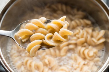 Makarna arka planında tam tahıllı fusilli bir kaşık, tencerede pişirilmiş. Sağlıklı beslenme.