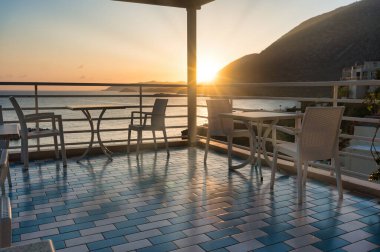 Batan güneş, yaz terasını deniz ve dağların zeminine karşı rahat masalar ve sandalyelerle aydınlatıyor. Seyahat daveti