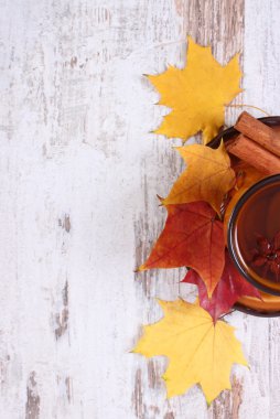 Cup of tea with lemon, spices and autumnal leaves on wooden background, copy space for text
