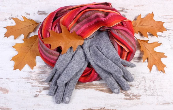 Womanly woolen clothes and autumnal leaves on old rustic wooden background — 图库照片