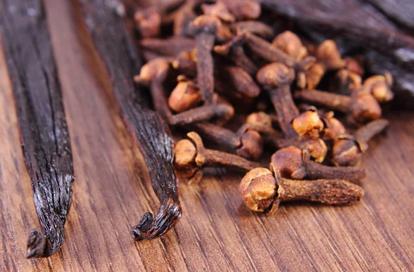 Closeup de cravos e baunilha perfumada na prancha de superfície de madeira — Fotografia de Stock